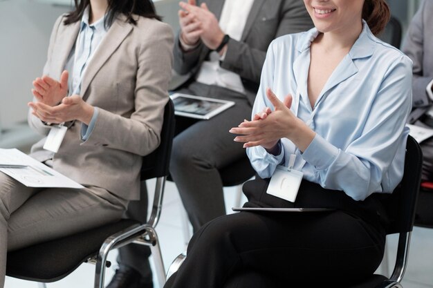 Closeup of two young female brokers applauding to speaker at conference