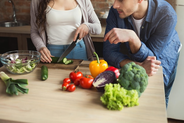 Closeup of unrecognizable couple cooking healthy food together in their loft kitchen at home. Cutting vegetables, preparing vegetarian salad, copy space