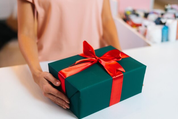 포장된 크리스마스 선물 상자를 들고 식별할 수 없는 여성의 손을 닫고 빨간 리본을 묶고