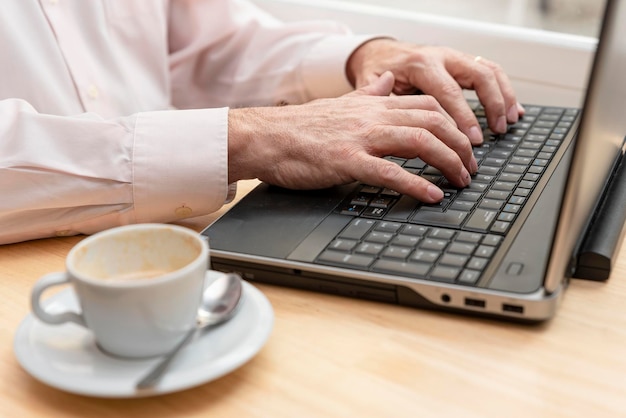 Closeup of an unrecognizable man hands typing on the keyboard of laptop a cup of coffee by his side