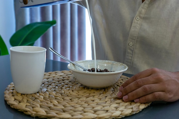 Closeup of unrecognizable man pouring milk and eating cereal for breakfast