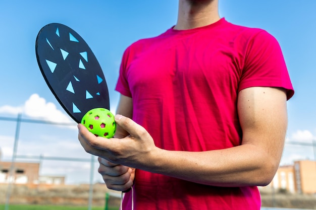 Foto primo piano di un giocatore di pickleball irriconoscibile che tiene la pagaia e la palla sul campo da gioco