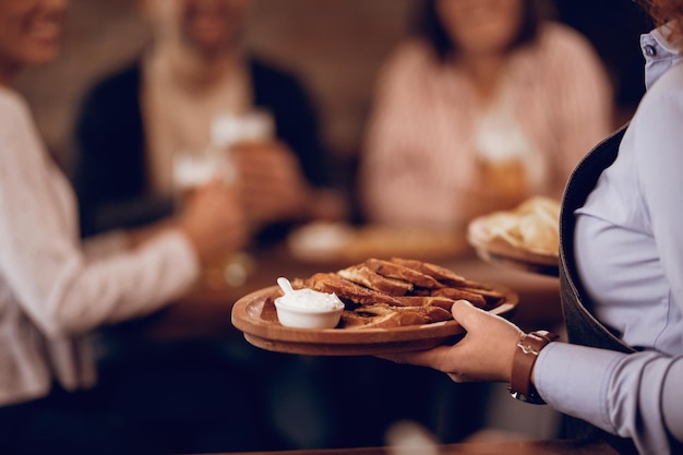 Foto primo piano di una cameriera irriconoscibile che porta cibo agli ospiti in un ristorante