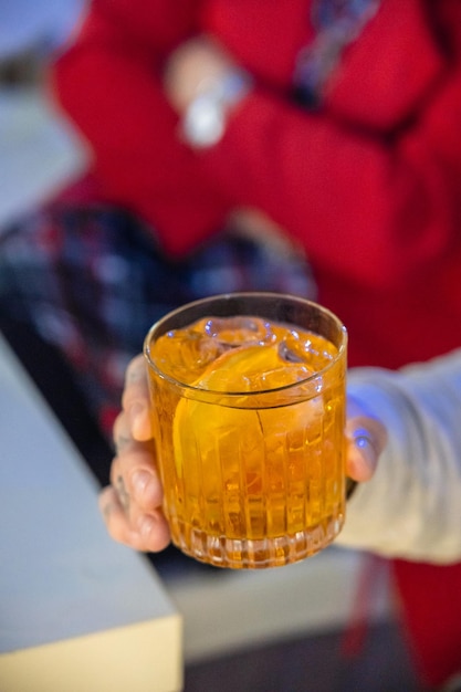 Foto close-up di un giovane irriconoscibile che tiene una bevanda alcolica arancione sulle rocce in un bar