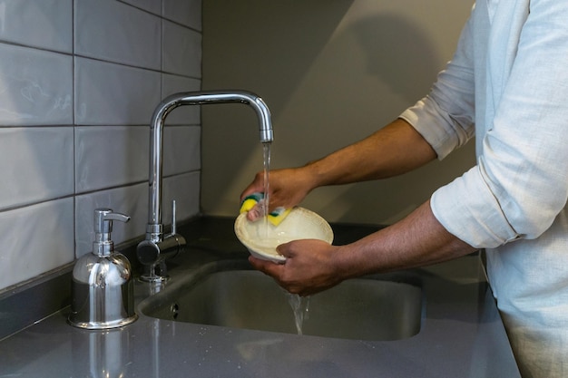 Крупным планом руки неузнаваемого молодого человека 39, когда он чистит посуду губкой с мылом и водой на кухне