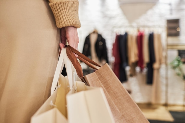 Closeup of unrecognizable young woman carrying bags with purchases in hand while shopping in clothing store copy space