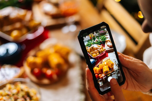 Photo closeup of unrecognizable young woman taking photo or making video of beautiful christmas dinner table on mobile phone