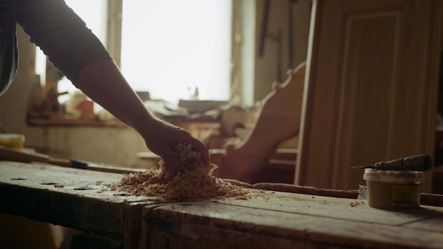 Closeup unrecognized man throwing sawdust in carpentry workshop Sawdust on wood lathe machine after work in studio Unknown handyman pouring sawdust indoors Male carpenter working alone