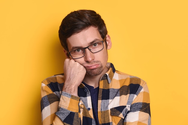 Closeup of upset tired guy propping his head with hand over yellow background