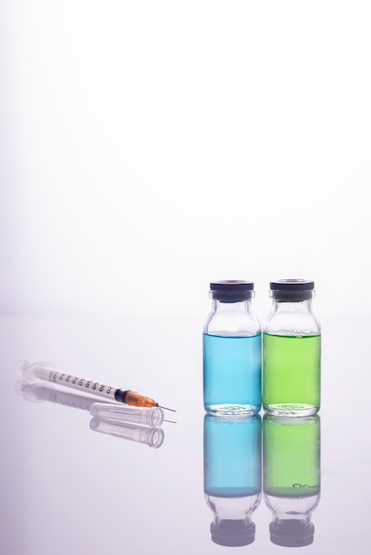 Foto vaccino del primo piano fiale di vetro con liquido multicolore e una siringa su sfondo bianco