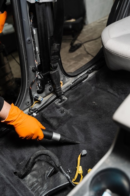 Photo closeup vacuum cleaning of dirty car floor with removed seats in detailing service worker of detailing service is using vacuum cleaner for remove dust and dirt in car