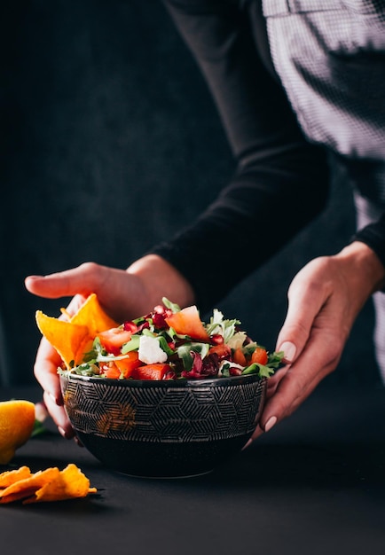 Primo piano su un'insalata di verdure in un piatto che viene servito sul tavolo da mani femminili su uno sfondo scuro