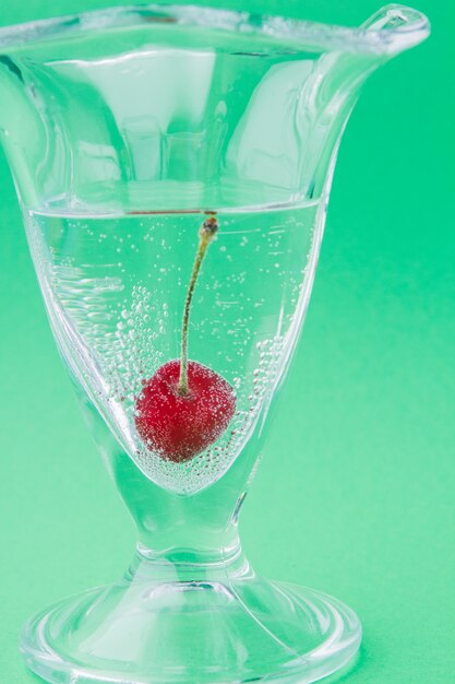 Foto tazza di vetro verticale del primo piano con acqua e una ciliegia