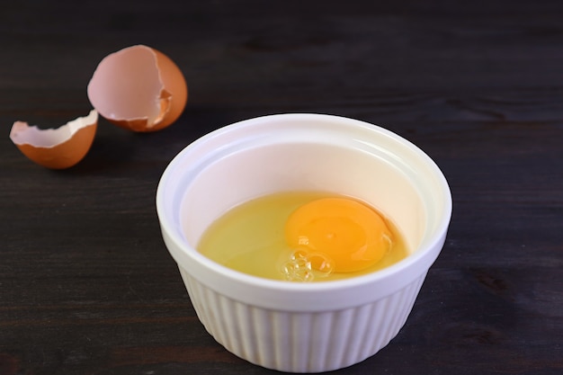 Closeup vibrant color raw egg in a bowl with blurry eggshell in background