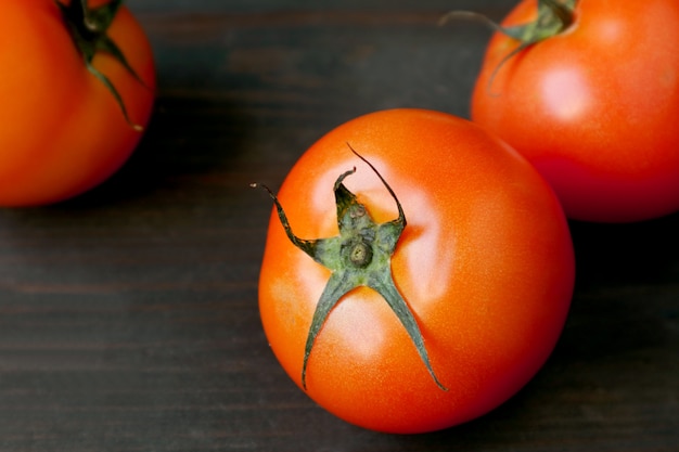 Closeup vibrant red tomatoes scattered on dark brown wooden background