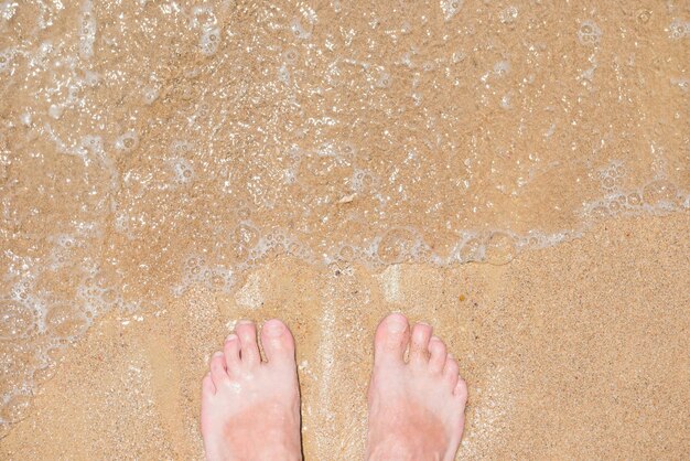 Vista ingrandita dei piedi umani nudi sullo sfondo della spiaggia di sabbia. concetto di vacanza estiva