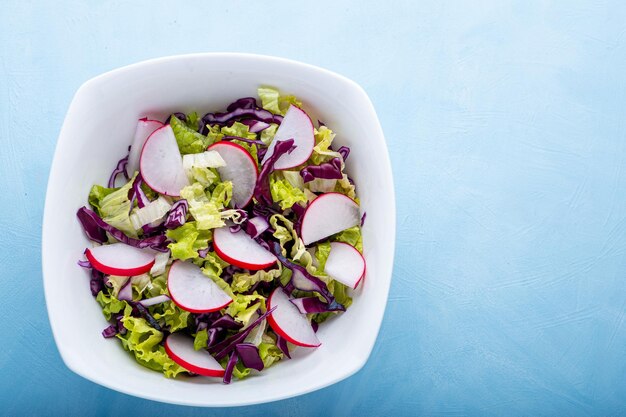 Closeup view of a bowl of green salad over blue backdrop