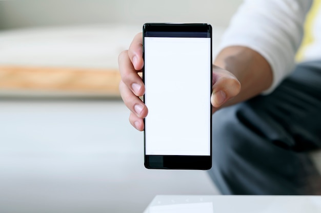 Vista del primo piano dell'uomo di affari che mostra il telefono cellulare dello schermo in bianco in ufficio.