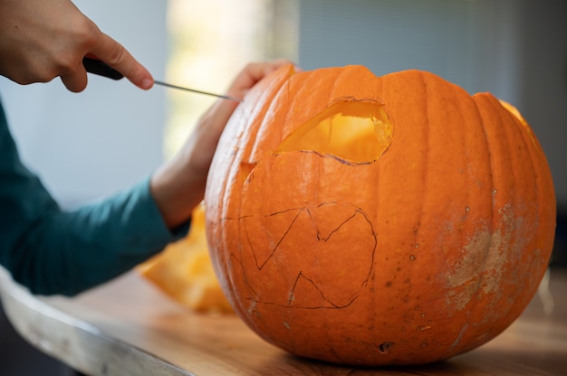 Closeup view of a child carving halloween pumpkin on a wooden table.