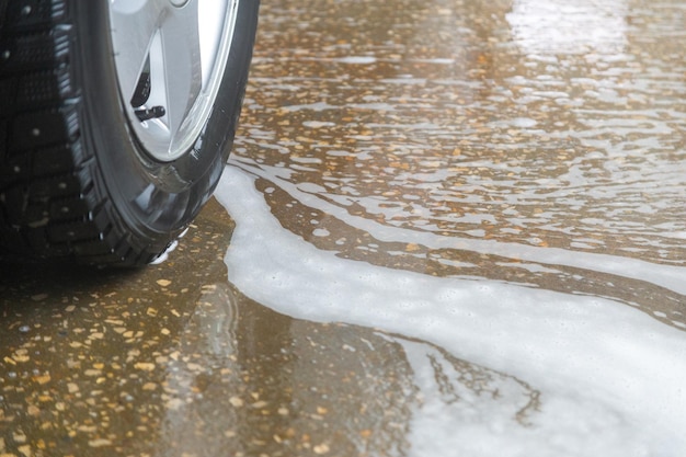 A closeup view of civil car wheel in soap puddle on the floor of washing garage