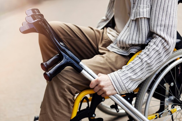 Closeup view crutches in the hands of a man A man sits in a wheelchair puts crutches on his knee holds them with his hand on the street