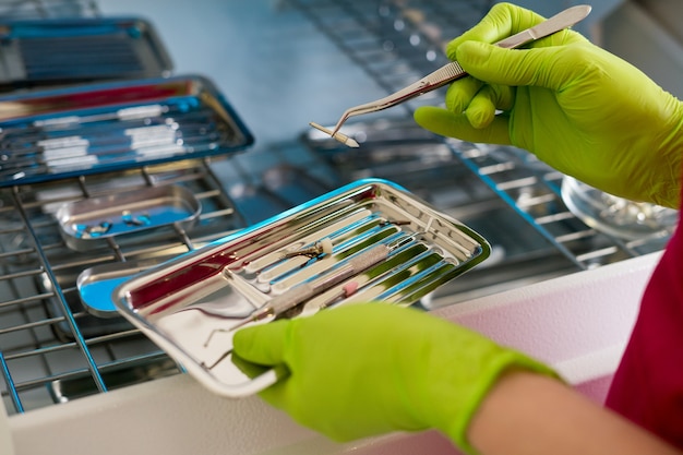 Крупным планом вид рук стоматолога в перчатках, держащих стоматологические инструменты и расходные материалы