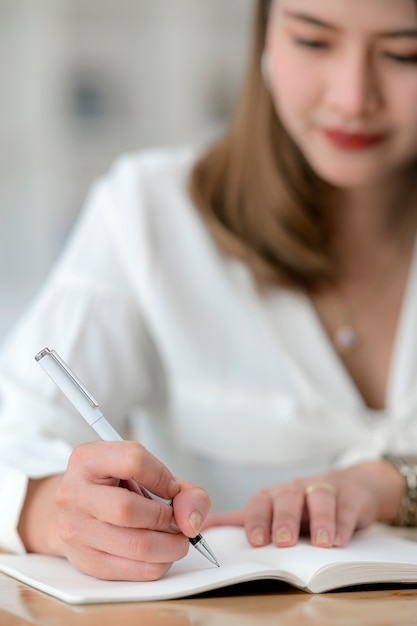 Closeup view of female hand with pen writing on diary.