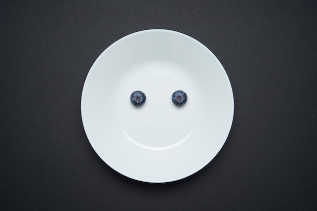 Closeup view of fresh two blueberry on white disc ,black background , smile and happy morning breakfast concept