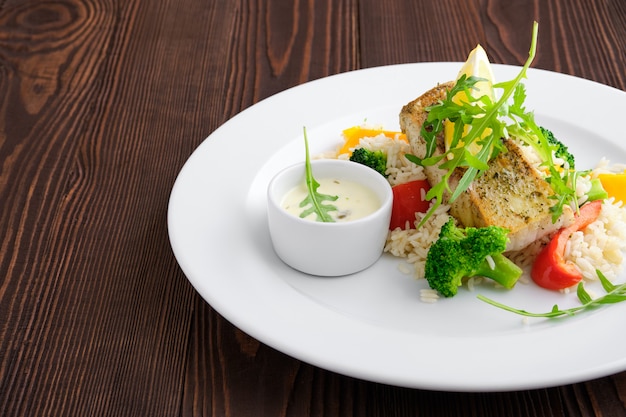 Closeup view of fried zander with rice, bell pepper and arugula served with mayonnaise sauce