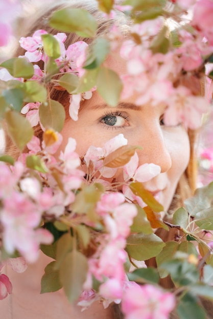 Vista ravvicinata di una ragazza con la pelle bianca e chiara attraverso la coppia di alberi di mele in fiore nel giardino concetto senza allergie e pelle perfetta