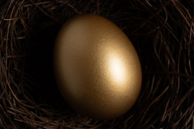 Photo closeup view of golden egg in nest on a dark table easter concept