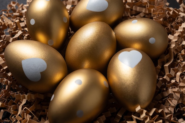 Photo closeup view of golden eggs in paper nest on a dark table