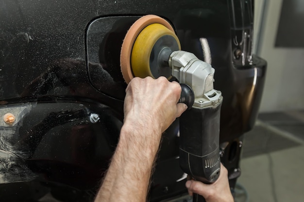 Closeup view on the hands of a male worker who holds a tool for polishing the fender of a car while working in a vehicle detailing workshop Auto service industry