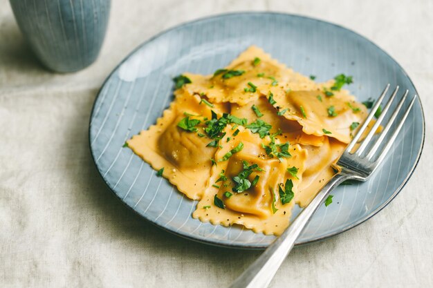 Closeup view of homemade Italian ravioli pasta with parsley on a blue ceramic plate