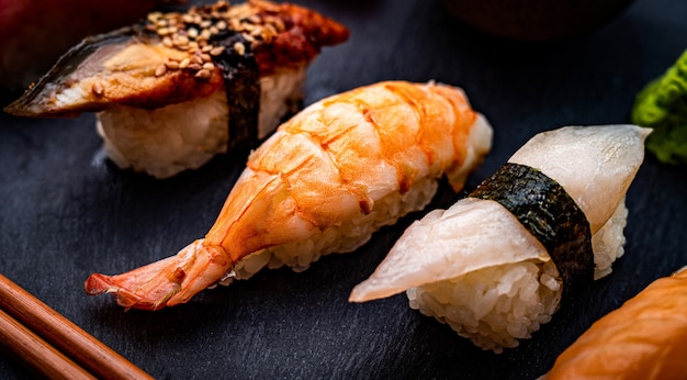 Closeup view on japanese sushi sashimi set with shrimps served with chopsticks and green wasabi on b...