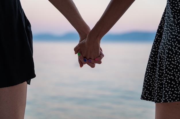 Closeup view of lesbian gay couple holding hands standing by the evening sea.