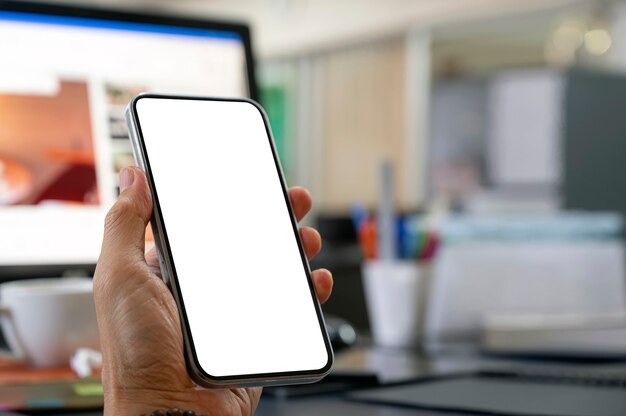 Closeup view of man hand holding blank screen smartphone with blurred office room backgound.