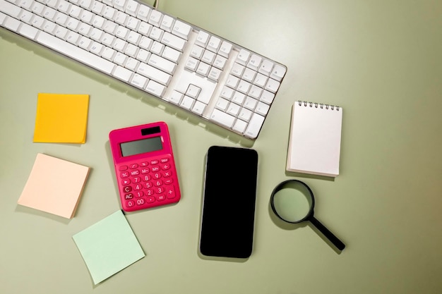 Closeup view of mobile phone with blank screen and an empty notebook and note paper with magnifying glass and calculator