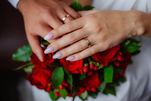 Closeup view of newlyweds hands holding colorful wedding bouquet bride and groom wearing wedding rin