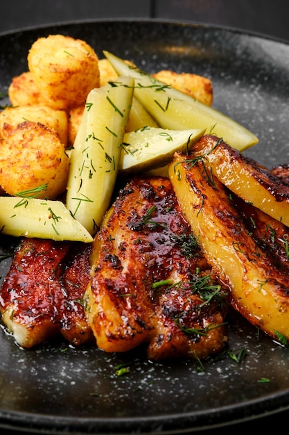 Closeup view of roasted pork belly with potato balls and pickled cucumber on a plate