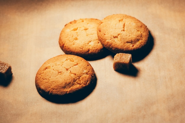 Foto primo piano di biscotti dolci croccanti rotondi con cubetti di zucchero di canna su sfondo di carta strutturata