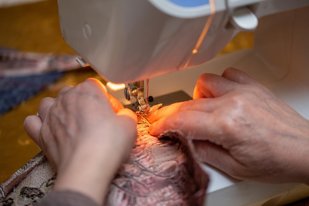 Крупный план процесса шитья руки пожилой женщины с использованием техники селективного фокуса швейной машины