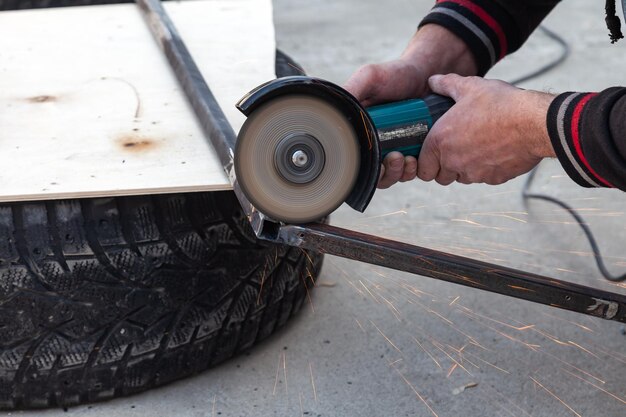 Closeup view strong man master without gloves on arms performs metal cutting with an angle grinder in the garage workshop blue and orange sparks fly to the sides