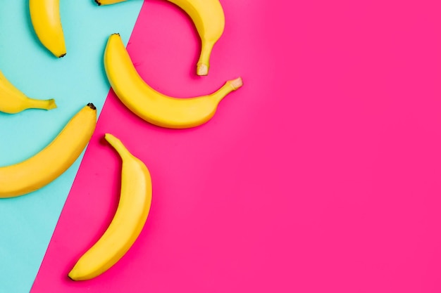 Photo closeup view of top yellow bananas on bed blue and pink background with copy space