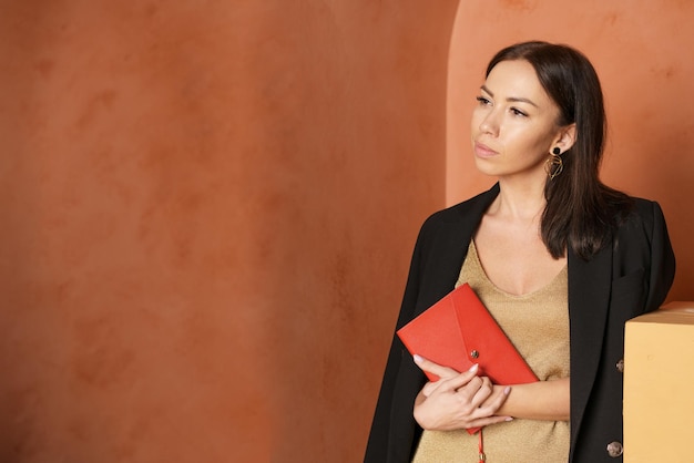 Primo piano di una donna che indossa una giacca nera e tiene in mano un libro con una copertina rossa vuota, spazio libero per te.