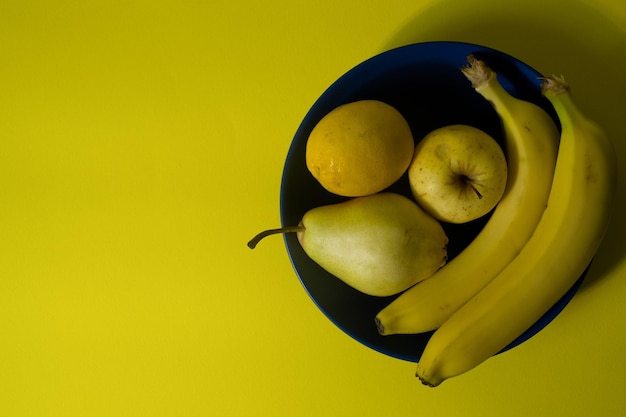 Closeup view of yellow banana apple pear and lemon on blue plate