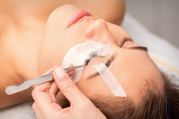 Closeup view of young woman having eyelash extension procedure in beauty salon