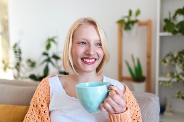 Closeup view of young woman with cup of hot drink at home blank space People drinks and leisure concept happy young woman with cup of tea or coffee at home