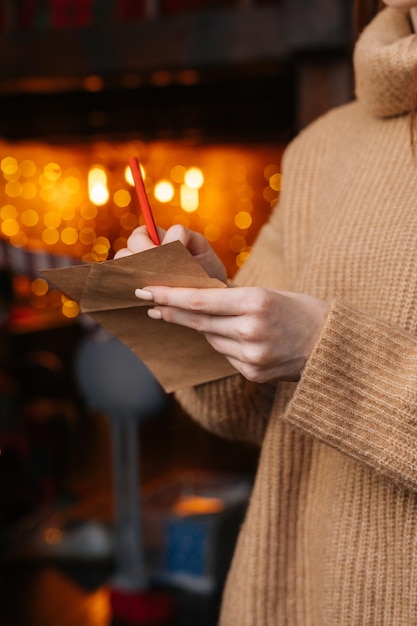 Closeup view of young woman writing Christmas letter to Santa Claus on background xmas tree