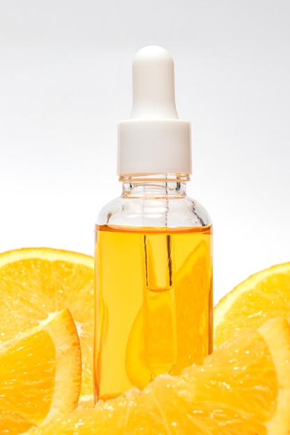 Клоуз-ап бутылки с сывороткой витамина С с каплями, окруженными свежими яркими оранжевыми кусочками